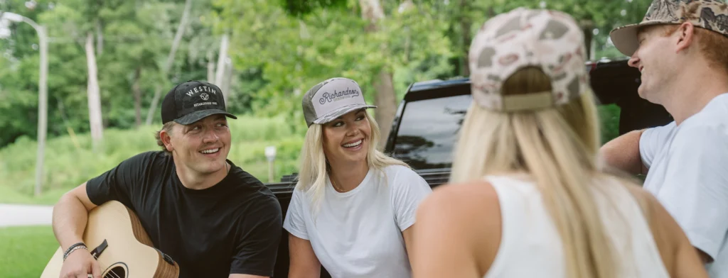 Group of friends hanging out, one playing guitar and all wearing custom Richardson hats