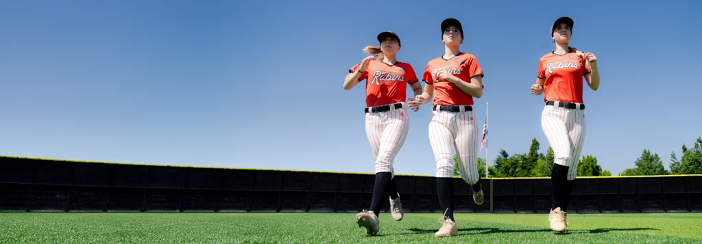 Softball players running on field wearing custom visors and uniforms by Richardson