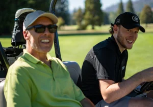 Two team members smiling in a golf cart during a company golf outing.